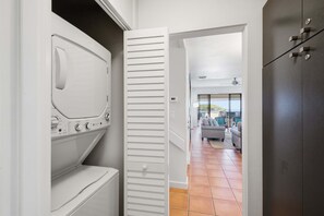 A laundry room with a washing machine and dryer, a white door leading to a living area with a sofa and a view of the outdoors. - Luxury Golf Villa in Kapalua Maui with Ocean and Sunset Views (Kapalua)
