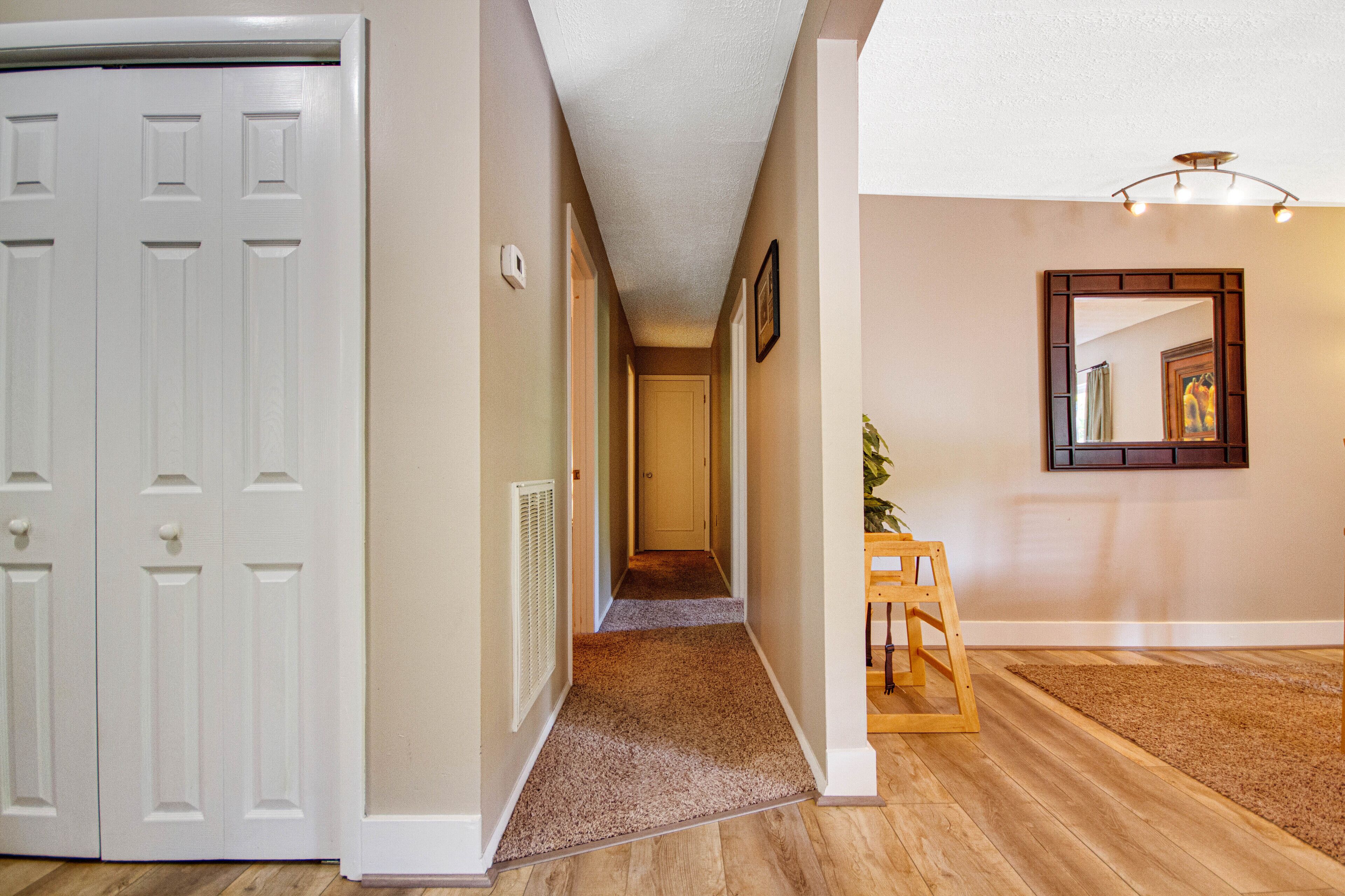 A hallway with a carpeted floor, a wooden bench, a white door, and a wall-mounted mirror.