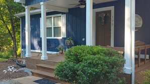 Una casa azul con porche, un árbol pequeño y un camino de entrada de grava.