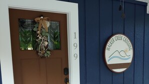 Una puerta principal con el número '199' sobre ella, un banco de madera a la derecha y un letrero que dice 'Walker Creek Crossing' con un gráfico de una ola y un sol.