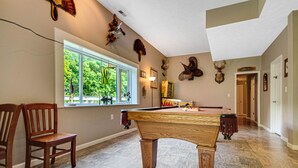 Una habitación amplia con mesa de billar, un ventanal grande y diversas decoraciones en la pared, incluyendo monturas de animales.