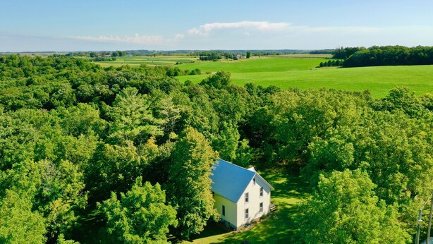 A white house with a blue roof surrounded by dense green trees and open fields. - *CLOSED FOR 2026 SEASON* Schmidt Farm: an interactive farm experience (Preston)