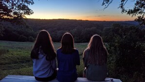 Three people sitting on a bench facing a sunset. - *CLOSED FOR 2026 SEASON* Schmidt Farm: an interactive farm experience (Preston)