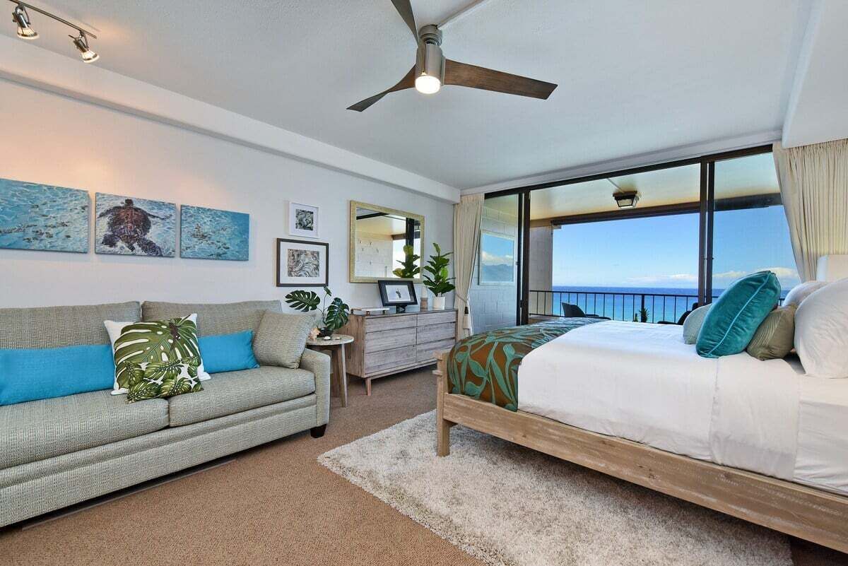 A spacious bedroom suite featuring crisp linens, tasteful artwork, and an expansive ocean view framed by sliding doors.