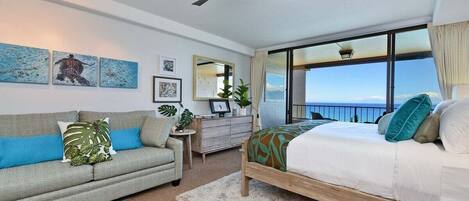 A spacious bedroom suite featuring crisp linens, tasteful artwork, and an expansive ocean view framed by sliding doors.