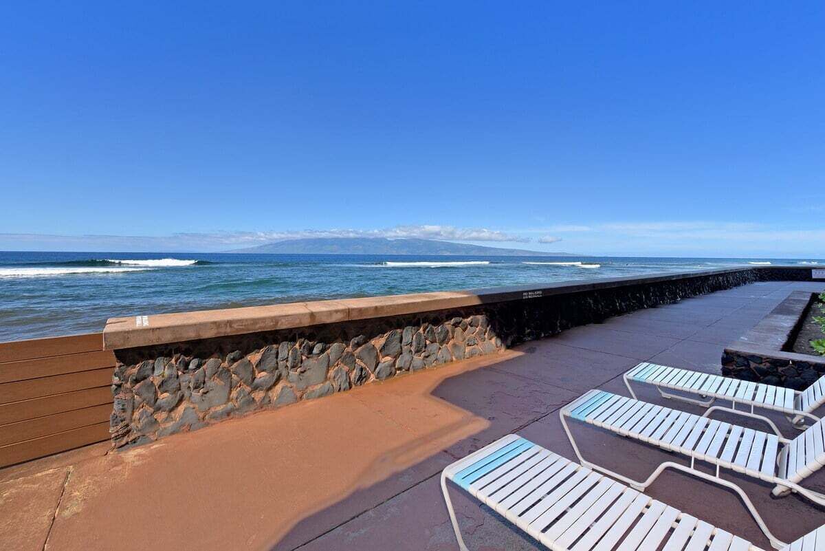 Une terrasse en bord de mer, dotée de chaises longues et d’un mur de pierre donnant sur l’océan.