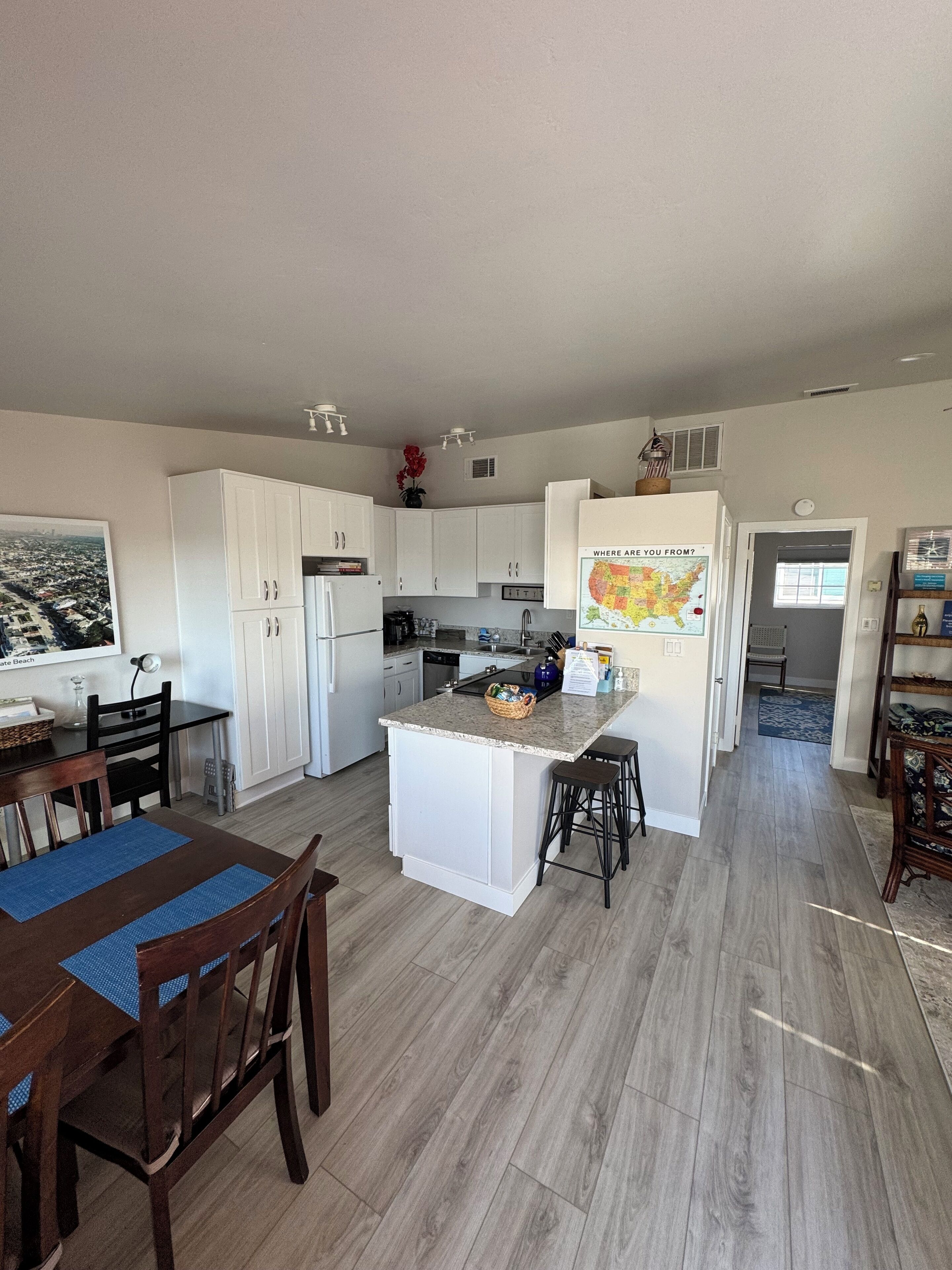 A modern kitchen with white cabinets, a central island, and a dining area with wooden chairs and a blue placemat.