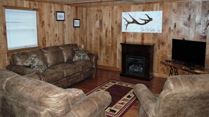 Una sala de estar con paneles de madera, una chimenea, sofás de cuero y un televisor.