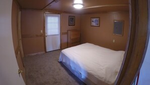 Un dormitorio con una cama individual, una puerta con ventana, un aparador y una lámpara en el techo.