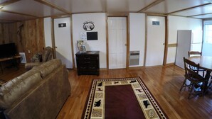 Amplia sala de estar con techo de madera, un sofá de cuero, una mesa de comedor con sillas y una alfombra estampada.