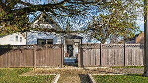A gated backyard with a wooden fence, a small building with a porch, and a yellow tactile paving path leading to the entrance. - Just off 6th Ave!  Beautifully Renovated Home! Close to UPS. (Tacoma)