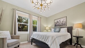 A bedroom with a bed, a chair, a bedside table, a lamp, and a window with curtains. - Just off 6th Ave!  Beautifully Renovated Home! Close to UPS. (Tacoma)