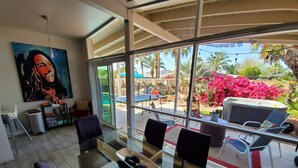 Habitació moderna amb taula de vidre, cadires, un quadre i vista a un pati exterior amb seients i plantes.