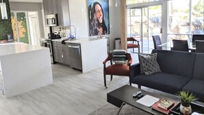 Un espai modern d'estar amb cuina, zona de menjador i una finestra gran que deixa entrar llum natural.