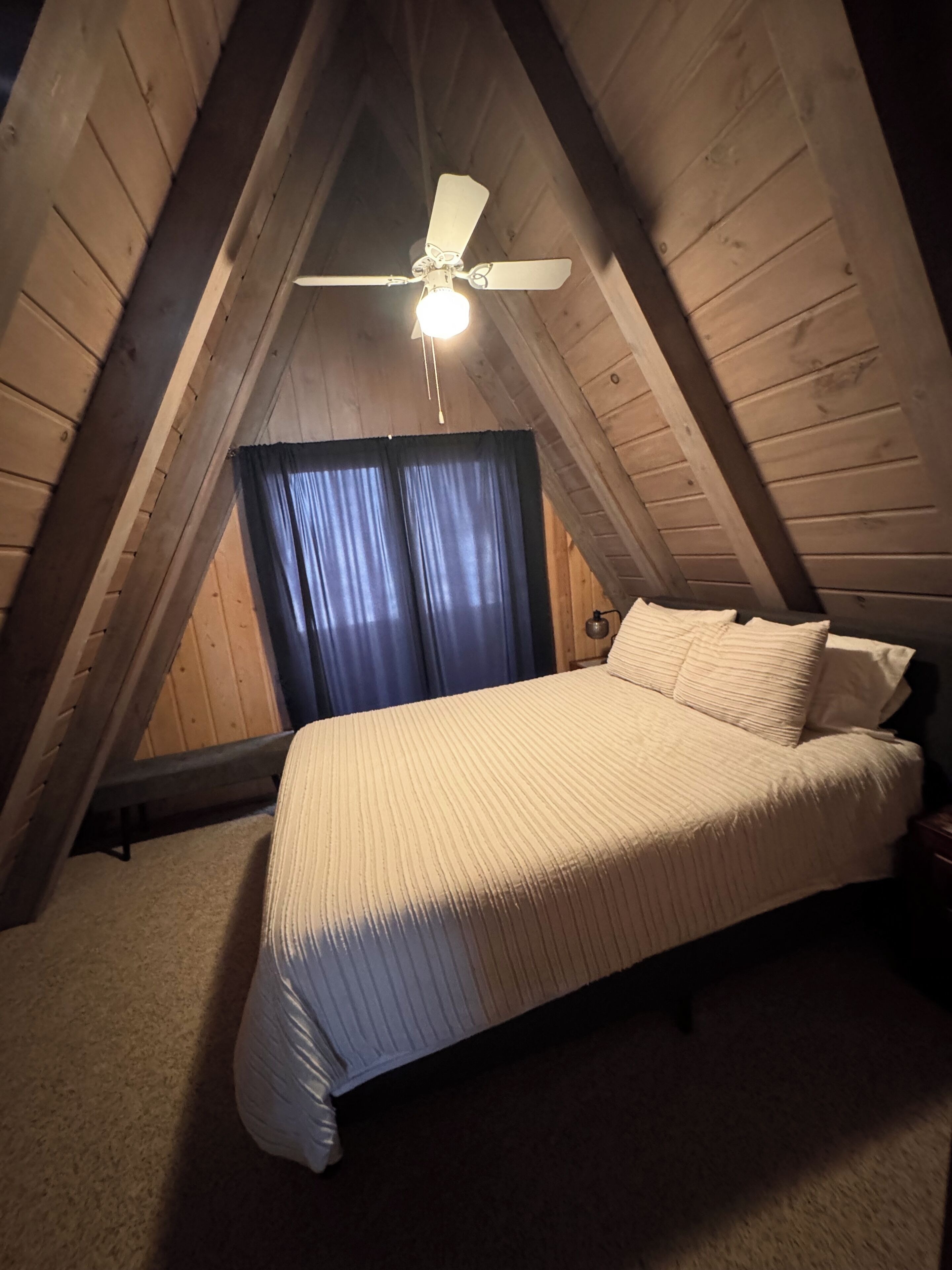 An attic bedroom with a bed, a ceiling fan, and wooden walls.