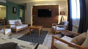 Una sala de estar moderna con un televisor de pantalla plana montado en una pared de madera, una mesa de centro y dos sofás con cojines estampados.
