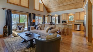 Ein geräumiges Wohnzimmer mit einer großen Couch, einem Couchtisch und einem Essbereich mit Stühlen. Die Küche ist sichtbar, mit Holzschränken und einem Edelstahlkühlschrank.
