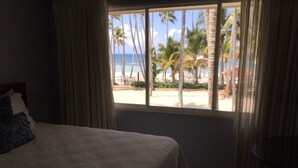 Une chambre avec un grand lit, une vue sur une plage bordée de palmiers et des rideaux à la fenêtre.