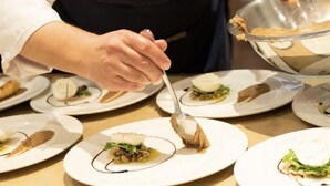 Un chef servant des plats à une table où sont disposées plusieurs assiettes.