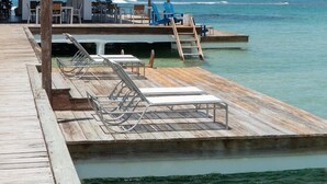 Une jetée en bois avec des chaises longues, une structure à toit de chaume et une vue sur l’océan.