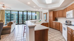 A modern kitchen with a large island, wooden cabinets, and a view of a residential area. - Phoenix on the Bay 1412 by Liquid Life (Orange Beach)