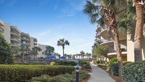 A pathway lined with palm trees and hedges, leading to a building with multiple balconies and a blue structure in the background. - Phoenix on the Bay 1412 by Liquid Life (Orange Beach)