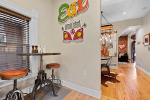 A dining area with a vintage VW bus wall art, a wooden table, and two stools.