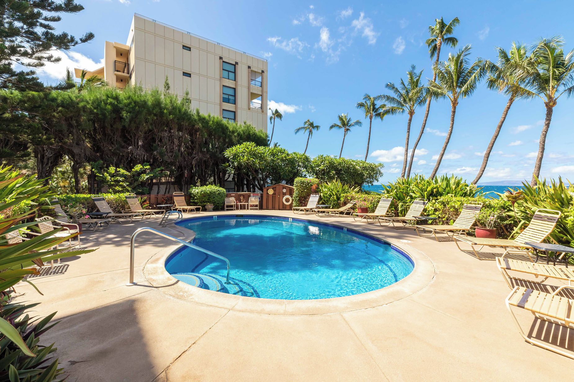 A pool area with lounge chairs, a clear blue pool, and a view of the ocean.