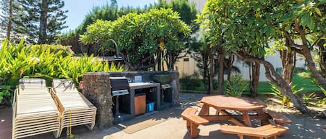 Un espacio al aire libre con un asador, sillas de lounge de madera y una mesa de picnic.