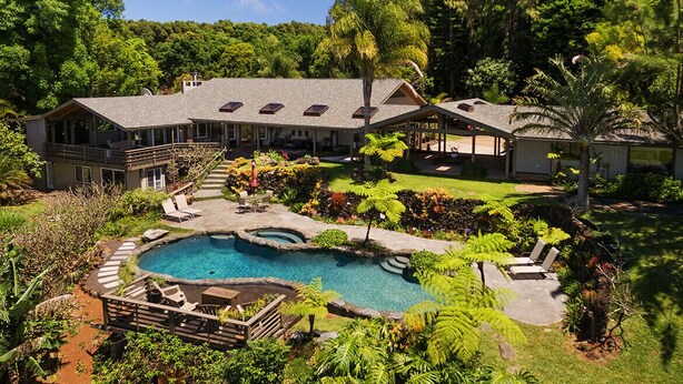 Une grande maison avec une piscine, entour ée d’une végétation luxuriante et d’un jardin bien entretenu.