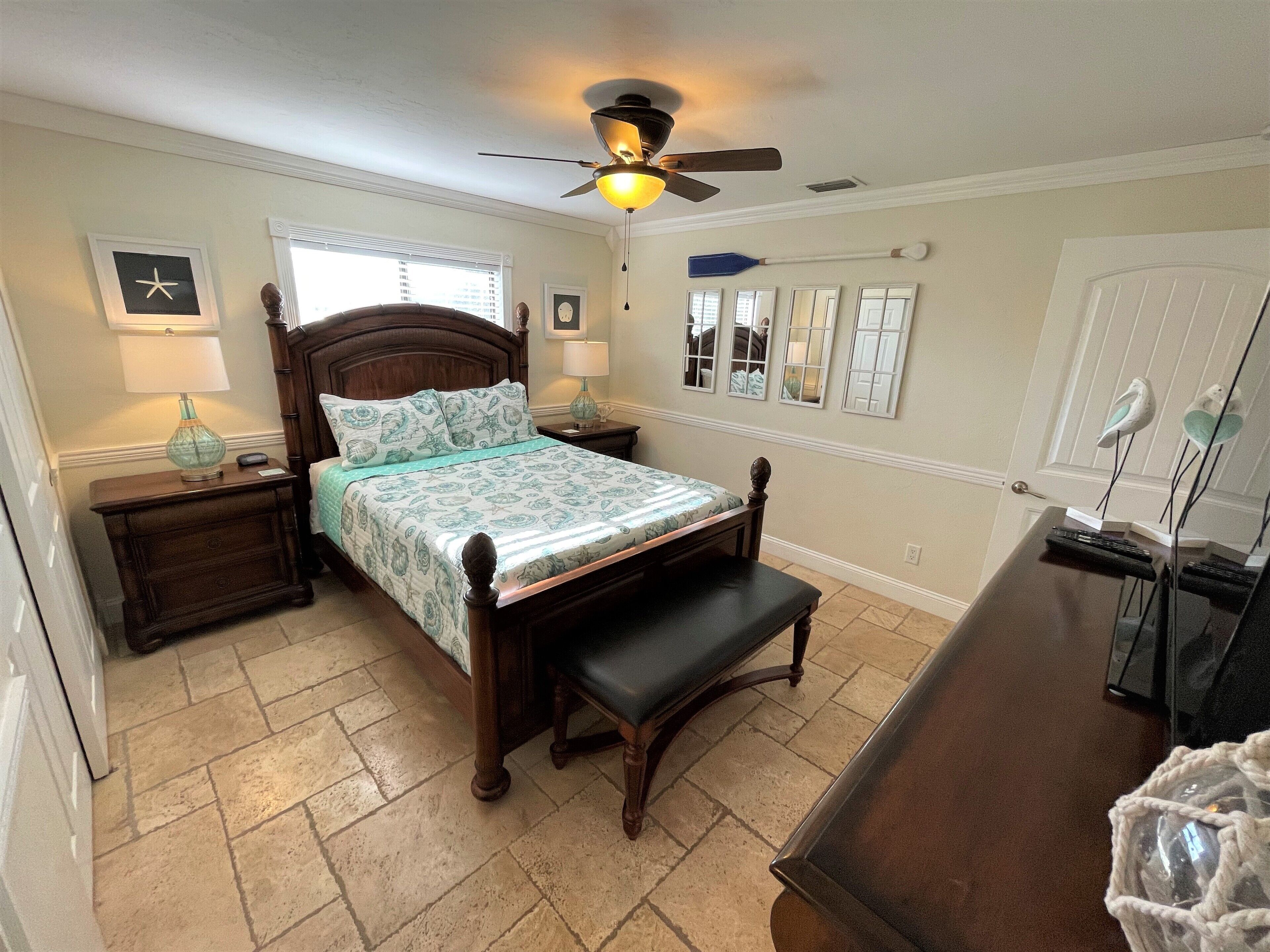 A bedroom with a wooden bed, a nightstand, a bench, a ceiling fan, and a dresser with a mirror.
