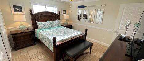 A bedroom with a wooden bed, a nightstand, a bench, a ceiling fan, and a dresser with a mirror.