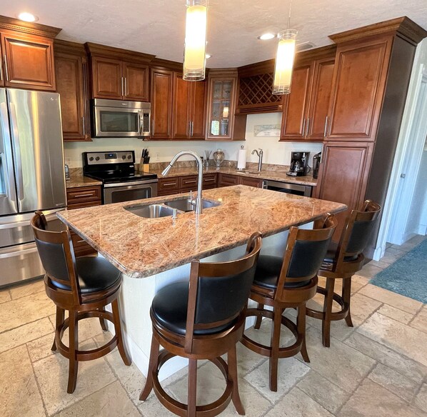 A kitchen with wooden cabinets, stainless steel appliances, a granite countertop, and bar stools. - The Seahorse Suite.  Welcoming guests back to Ft Myers Beach!  2 bedroom, 2 bath (Fort Myers Beach)