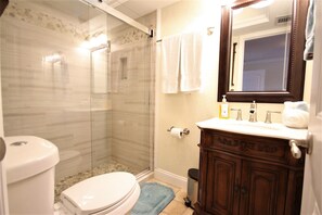A bathroom with a glass shower enclosure, a toilet, a sink with a mirror, and a blue bath mat. - The Seahorse Suite.  Welcoming guests back to Ft Myers Beach!  2 bedroom, 2 bath (Fort Myers Beach)