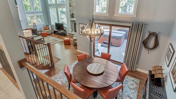 Uma sala de estar ampla, com uma grande mesa de jantar de madeira, assentos confortáveis, lareira e janelas grandes que oferecem vista para o exterior.