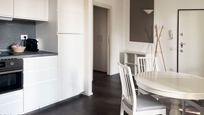 Een moderne keuken met witte kastjes, een zwarte koffiezetapparaat en een eethoek met een witte tafel en stoelen.