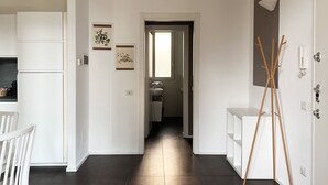 Een gang met aan één kant een keuken, een badkamer met raam, en een deur met een lamp.