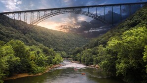 Une rivière traversée par un pont, bordée d’une forêt dense.