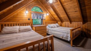 Une chambre confortable située dans les combles, avec deux lits, une fenêtre avec des rideaux, un ventilateur de plafond et une table de chevet.