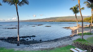 A beach with a grassy area, two lounge chairs, and a view of the ocean and hills. - Serene 3BR Puako Estate P10D – Beachfront Access & Tranquil Living (Kamuela)
