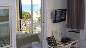 A room with a bed, a TV mounted on the wall, and a view of the ocean through a large window. - FLASH SALE:  Beautiful Beach Front Location (Carolina, Isla Verde)