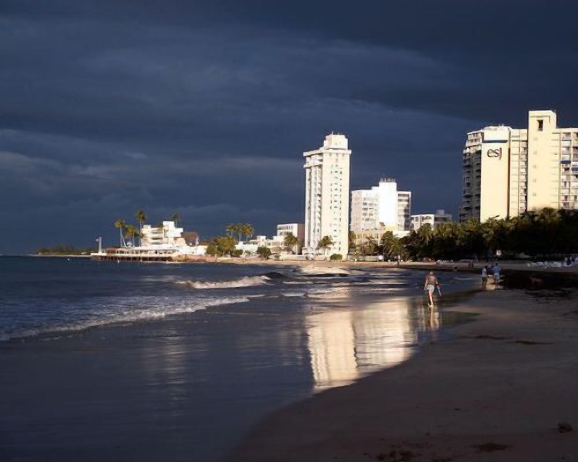 A coastal cityscape with high-rise buildings, a beach, and a boat in the water.