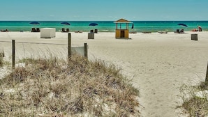 A beach with a lifeguard tower, beach chairs, umbrellas, and a sandy path. - Pet Friendly Ground Level Steps to the Sand! Pool Hot Tub WIFI (Panama City Beach)