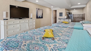 A hotel room with a large TV, a minibar, a kitchen area, and a bed with patterned bedding. - Pet Friendly Ground Level Steps to the Sand! Pool Hot Tub WIFI (Panama City Beach)