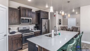A modern kitchen with dark wood cabinets, stainless steel appliances, a large island with a sink, and pendant lighting. - Estancia S304 Poolside Getaway Pool (St. George)