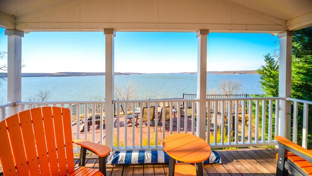 Une terrasse en bois offrant une vue sur un lac, avec des chaises orange et une petite table.
