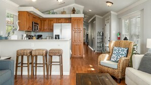Une cuisine moderne avec des meubles en bois, un îlot central doté de tabourets et un fauteuil en osier dans l’espace de vie, avec vue sur la cuisine.