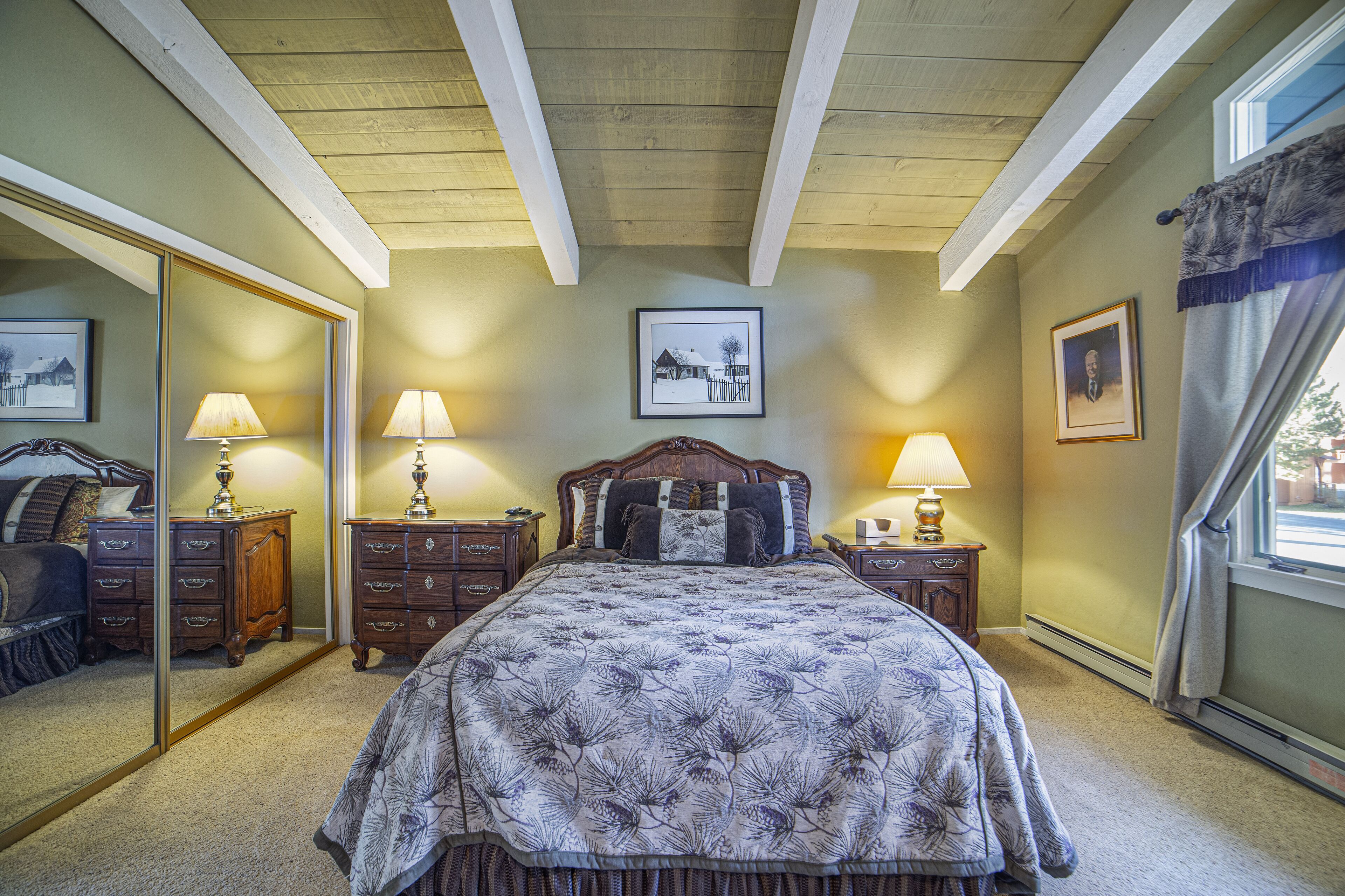A bedroom with a large bed, two nightstands with lamps, a dresser, a mirror, and a window with curtains.