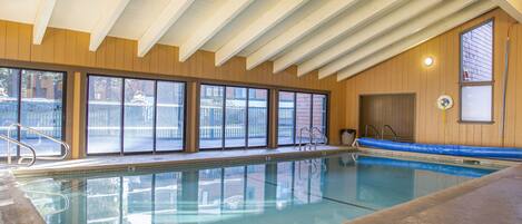 Piscina interna con ampie vetrate, pareti in legno e soffitto alto.