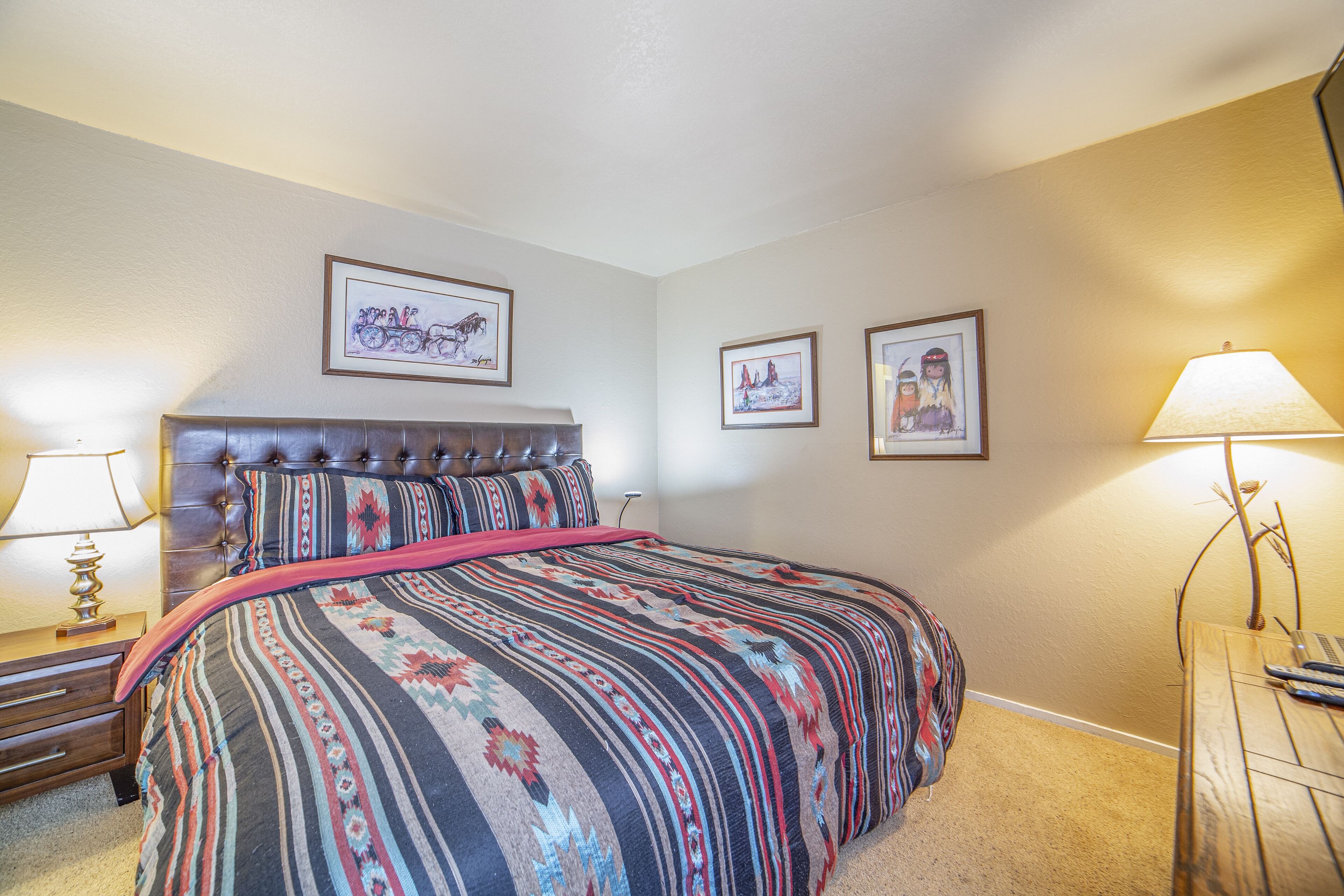 A bedroom with a large bed, a headboard, two bedside tables with lamps, and framed artwork on the walls.